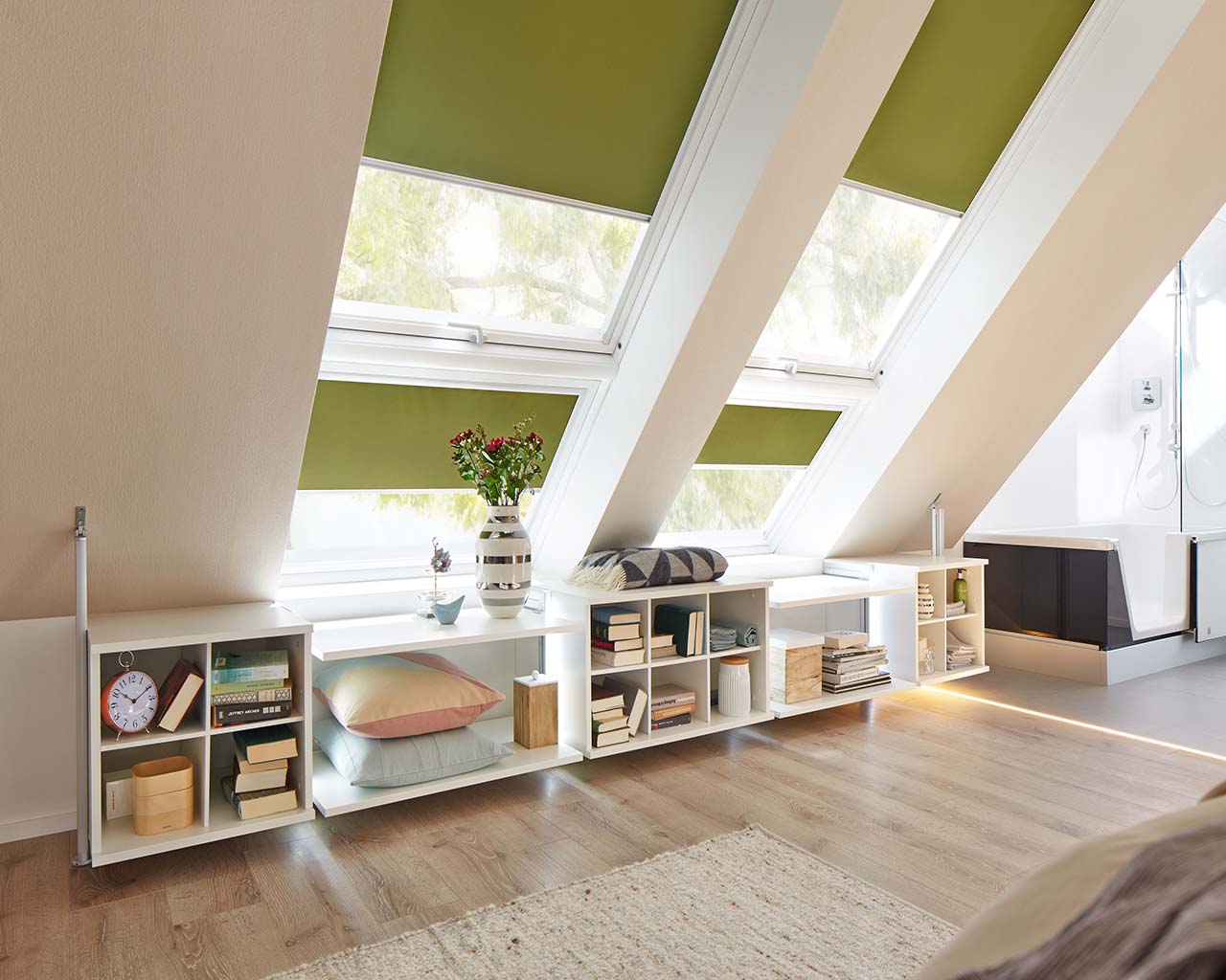 Gemütliches Loft mit Bücherregalen unter einer Dachschräge mit einem großen Dachfenster, das für natürliche Beleuchtung sorgt und einem offenen Bad.